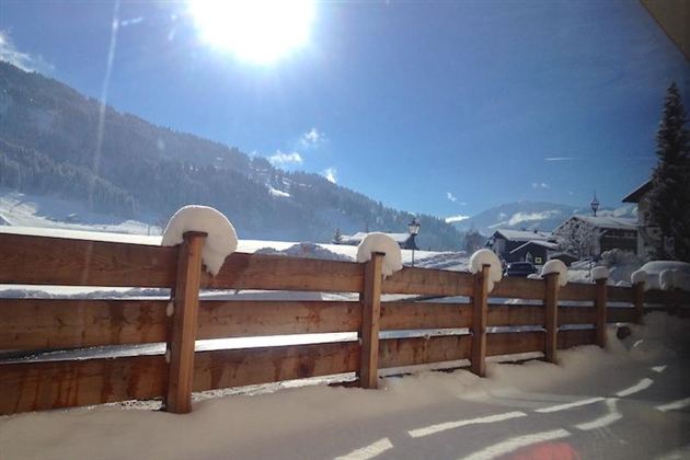 Eine verschneite Garten mit einem Holzzaun im Vordergrund. Die Sonne scheint hell über die Berge und den Schnee.