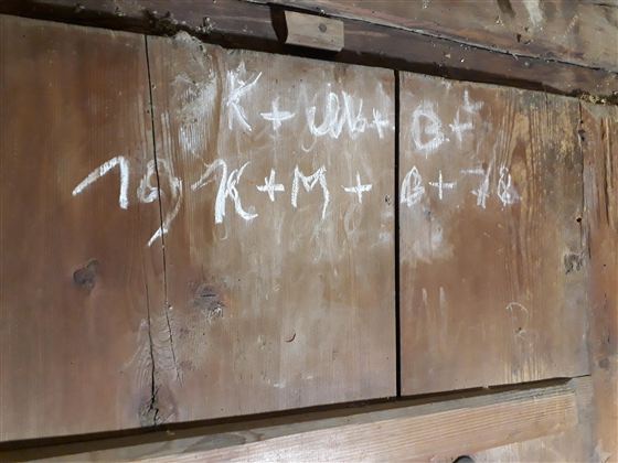 Eine Holzoberfläche mit handgeschriebenen Zeichen und Formeln in weißer Farbe. Die Inhalte scheinen mathematische Notationen oder Notizen zu sein.