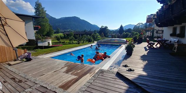 Ein schöner Pool in einer sonnigen Landschaft. Menschen genießen das Wasser und die Aussicht auf die Berge.