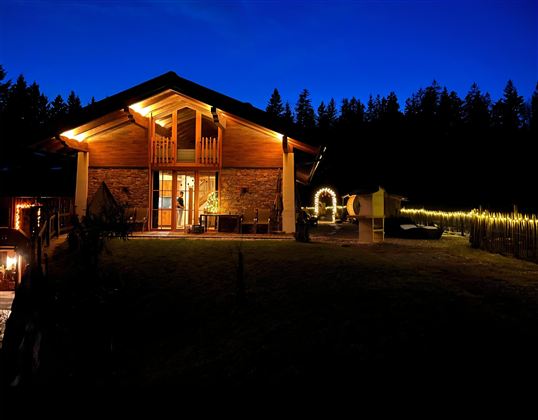 Das Almchalet Weberhof mit warmem Licht im Dunkeln. Der Garten ist gemütlich und von Bäumen umgeben.