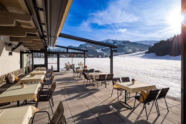 A cozy outdoor area with tables and chairs. In the background, one can admire the Kirchberg mountain world.