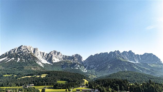 An impressive mountain landscape with high peaks and a clear sky. The green meadow in the foreground complements the picturesque panorama.