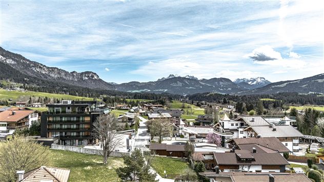 A picturesque landscape with a small village amidst mountains. The sky is clear and the surroundings are green and inviting.