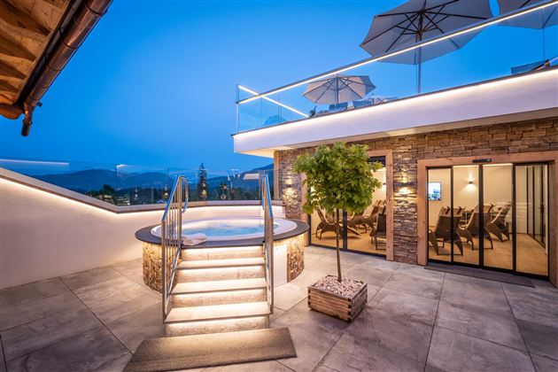 A modern terrace with a hot tub and cozy seating. The sky is blue and evening is approaching, creating a relaxed atmosphere.