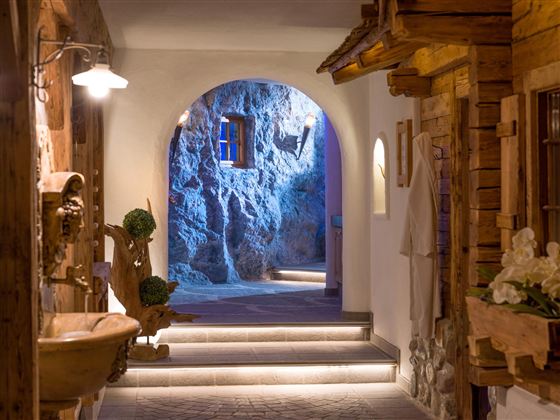 A cozy hallway with an arched entrance and soft lighting. Wooden details and natural elements are visible on the walls.