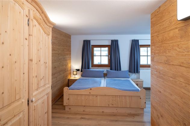 A cozy bedroom with wood paneling and a double bed. Large windows and curtains create a bright atmosphere.