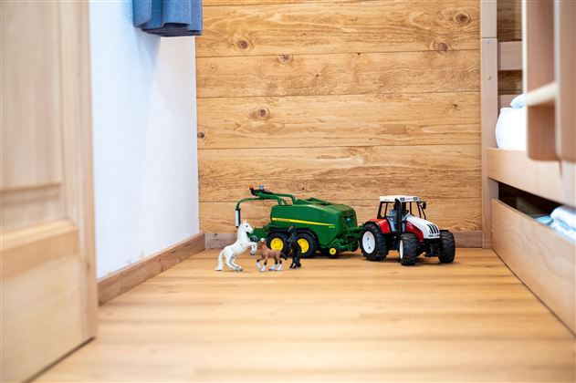 A toy landscape with a green tractor, a red tractor, and some plastic figures. The floor is made of wood and the wall is painted light.