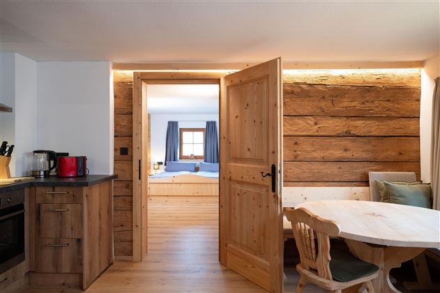 A cozy apartment with wood paneling and modern kitchen equipment. The room is bright and inviting, with access to a bedroom.
