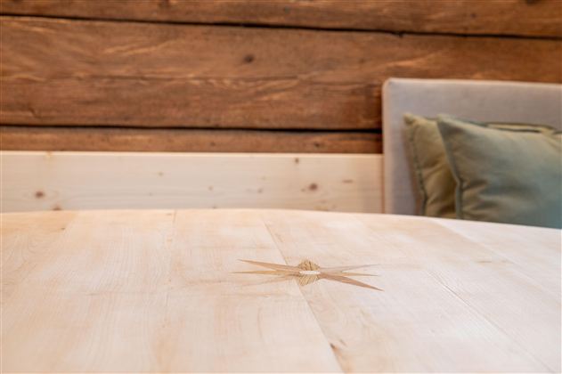 A beautiful wooden table with a unique grain. In the background, a cozy couch with cushions can be seen.