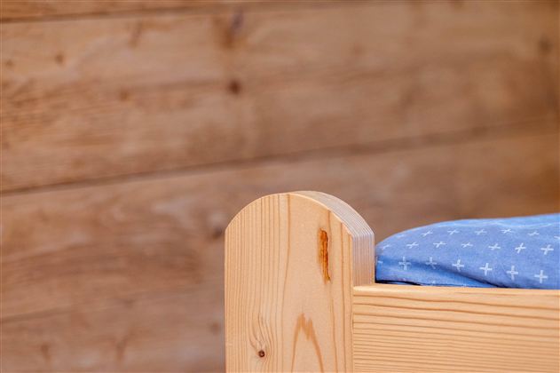 A part of a wooden bed frame with a blue bedspread. In the background, a wooden wall is visible.