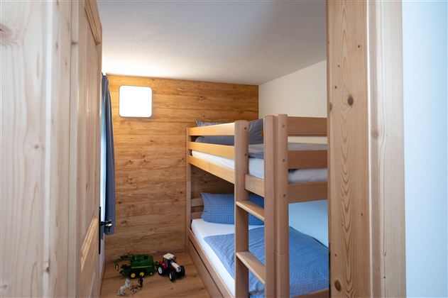 A cozy children's room with a wooden bunk bed. There are toys on the floor and soft, blue bedding.
