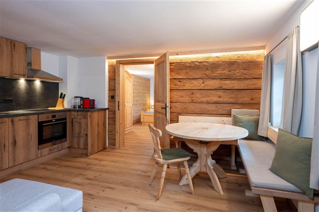 A cozy living kitchen made of wood with modern furnishings. The room has a round table and a comfortable seating area.