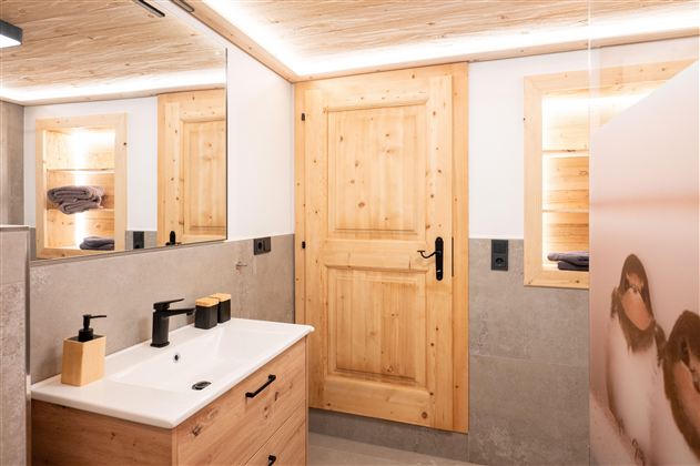 A modern bathroom with a wooden door and a white sink. The walls are light with warm wood elements and gentle lighting.