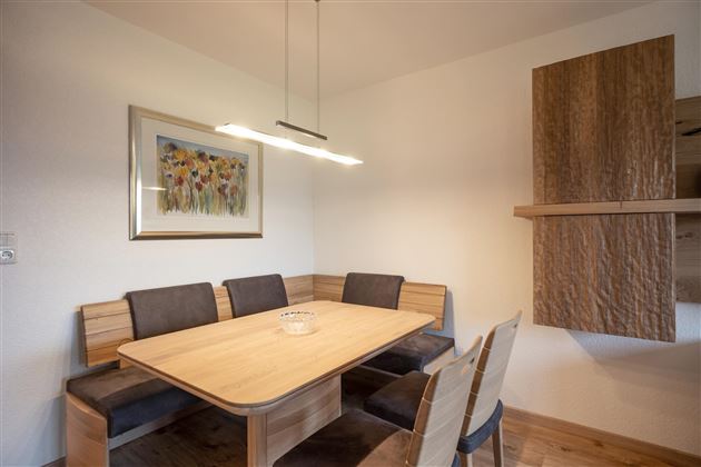 A modern dining area with a wooden table and comfortable benches. A painting with colorful flowers hangs on the wall.