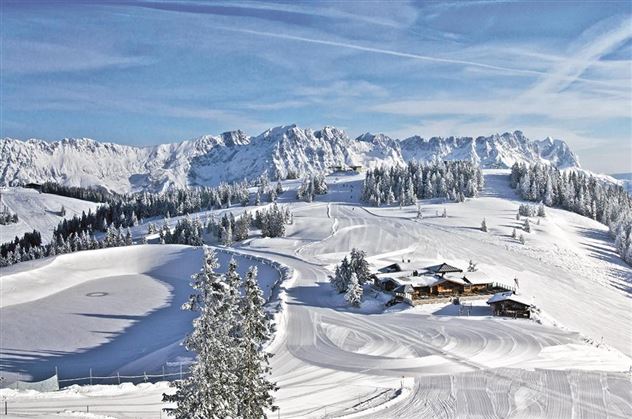 A snow-covered landscape with mountains in the background. In the foreground, there are slopes and a cozy cabin.