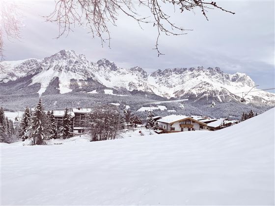 A snowy landscape with majestic mountains in the background. In the foreground, there are some cozy wooden houses.