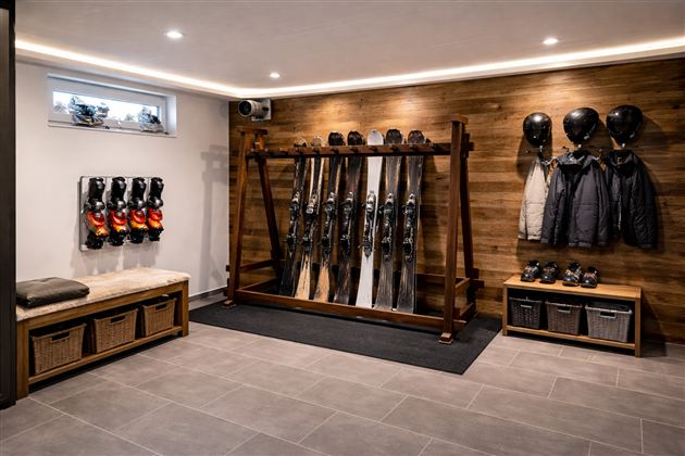 Een stijlvolle skikamer met ski's, skischoenen en helmen aan de muur. De houten bekleding en heldere verlichting creëren een gezellige sfeer.