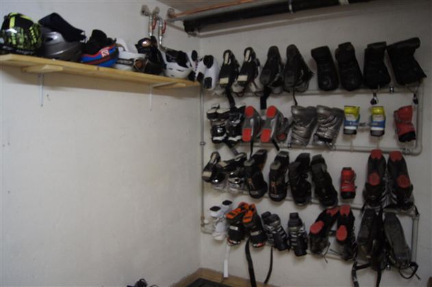 Ein Raum mit verschiedenen Ski- und Snowboardschuhen, die ordentlich an einer Wand hängen. Oben ist ein Regal mit weiteren Paaren von Schuhen.