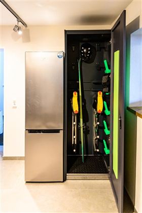 A modern ski room with a refrigerator and equipment storage. Skis, helmets, and ski rollers are neatly organized.