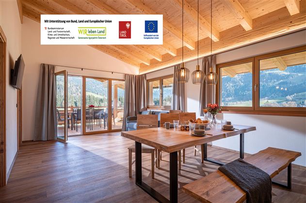 Ein modernes Esszimmer mit Holzinterior und großen Fenstern. Der Tisch ist gedeckt und bietet einen Blick auf die umliegenden Berge.