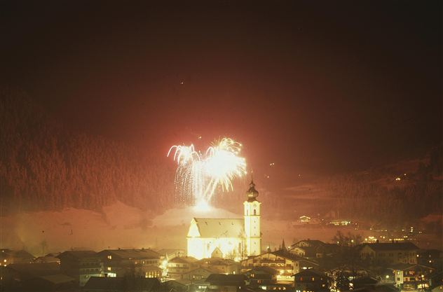 Ein Feuerwerk über einer malerischen Stadt im Winter. Die Kirche strahlt im Licht der bunten Feuerwerkskörper.