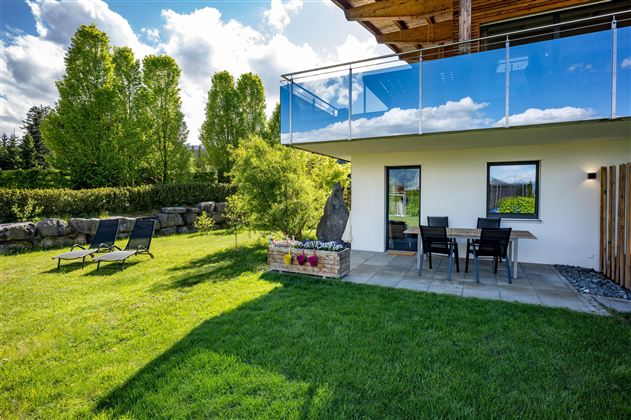 A modern house with a balcony and a cozy terrace. The garden is green and inviting, perfect for relaxation.