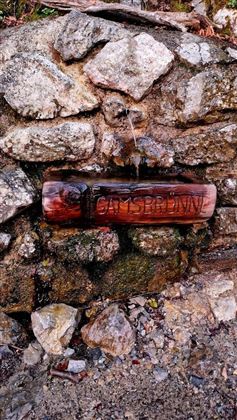 Een rustieke houten bron is in een stenen gevel geïntegreerd. De naam "Gaisbrunn" is duidelijk in het hout geschnitzt.