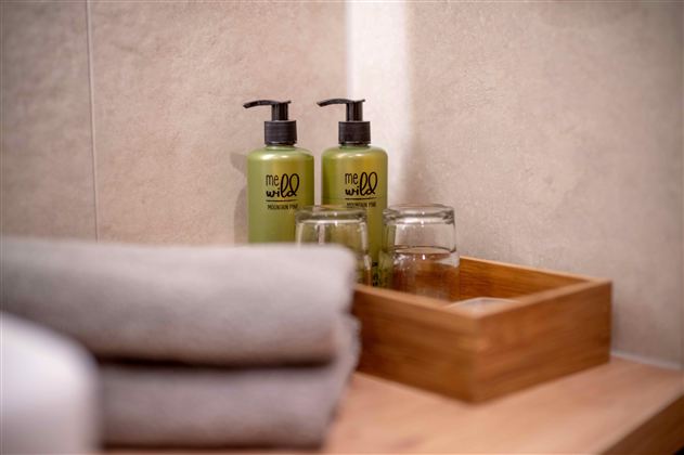 Two green care products stand next to glasses on a wooden tray. In the background, freshly folded towels are visible.