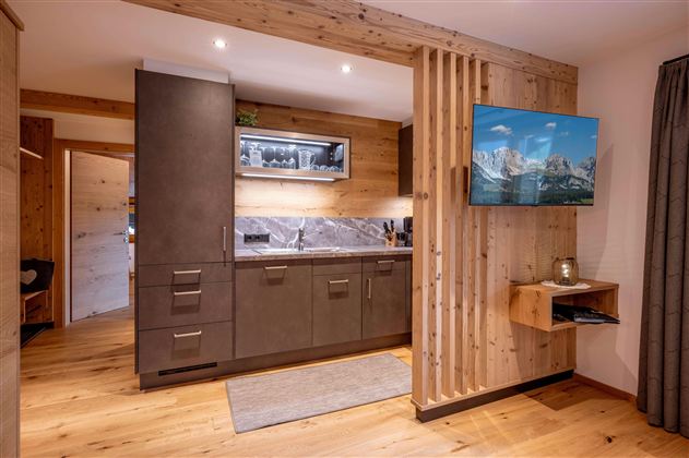 A modern kitchen with wood paneling and stylish appliances. A television displays a mountain landscape on the wall.