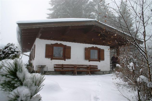 A cozy wooden house in a wintry landscape. The snow covers the ground and surrounds the house in a misty atmosphere.