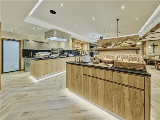 Ein modernes Restaurant mit hellen Holzregalen und einer offenen Küche. Auf der Anrichte sind frisch gebackenes Brot und andere Speisen angerichtet.