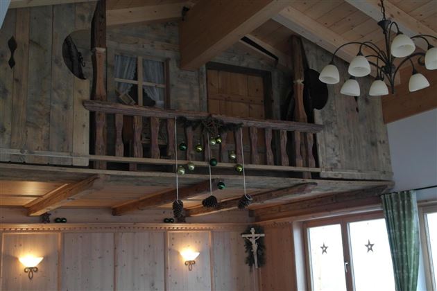 Een gezellige woonruimte met houten wanden en een open bovenverdieping. Aan het plafond hangen lampen en een feestelijke decoratie.