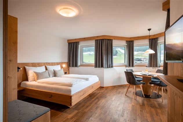 Ein modernes Hotelzimmer mit Holzdekor und großen Fenstern. Es bietet ein Doppelbett, einen Tisch und Stühle sowie einen Blick auf die grüne Landschaft.