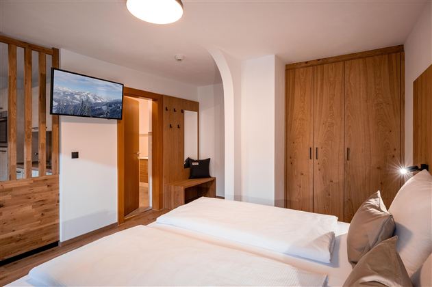 Ein helles Schlafzimmer mit zwei Einzelbetten und einem modernen Kronleuchter. Durch das Fenster sichtbar ist eine grüne Außenansicht.