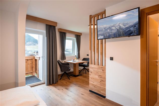 Ein gemütliches Zimmer mit zwei Einzelbetten, einem Schreibtisch und einem Fernseher. Durch die Fenster ist viel Tageslicht zu sehen.