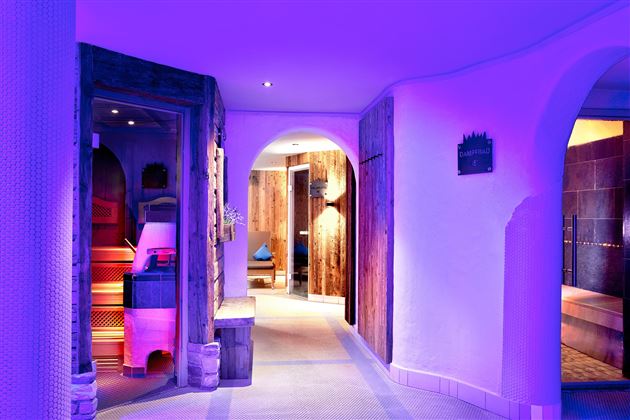 A modern wellness area with soft lighting in shades of purple. The hallway leads to various relaxing rooms.