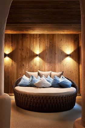 A cozy round seating area with many cushions. The walls are made of wood, and warm light creates a relaxed atmosphere.