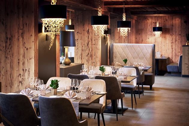An elegant restaurant with wooden paneling and stylish lamps. The tables are thoughtfully set and create an inviting atmosphere.