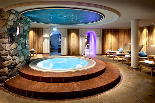 An elegant wellness area with a round hot tub in the center.  
Surrounded by comfortable loungers and warm light, this space invites relaxation.