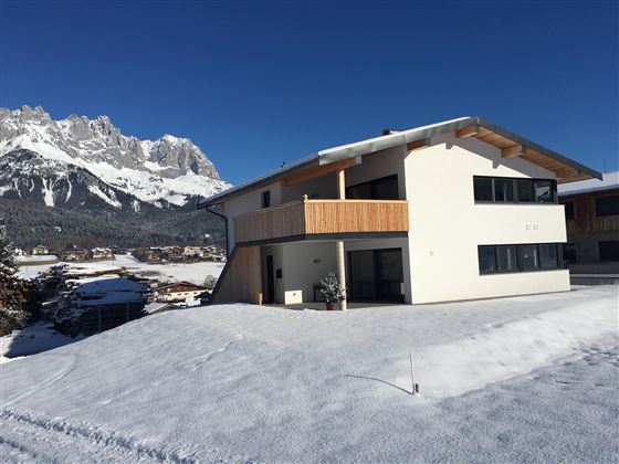 A modern house in a snowy landscape. In the background, impressive mountains can be seen.