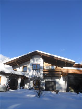 Een mooi huis in de sneeuw met een heldere blauwe lucht. De omgeving is winterachtig en vredig.