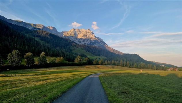 Een schilderachtig landschap met zachte heuvels en majestueuze bergen op de achtergrond. Een rustige weg loopt door de weelderige weilanden.