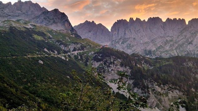 Een indrukwekkend berglandschap met steile rotsen en weelderig groen. De lucht vertoont zachte kleuren bij zonsondergang.