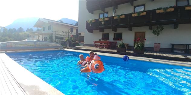 Ein einladender Schwimmingpool mit Kindern, die auf einem aufblasbaren Spielzeug schwimmen. Im Hintergrund sieht man ein charmantes Haus und die umliegende Landschaft.