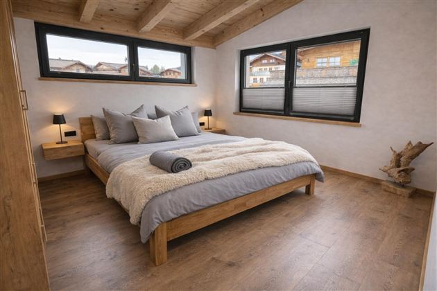 Ein gemütliches Schlafzimmer mit einem Holzbett und weichen Kissen. Große Fenster bieten einen Blick auf die Umgebung und lassen viel Licht herein.