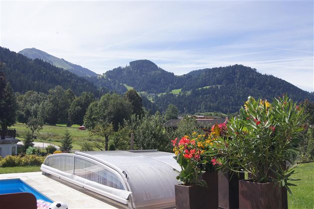 Ein schöner Ausblick auf Berge und grüne Wiesen. Im Vordergrund stehen blühende Pflanzen und ein Pool mit einer Abdeckung.