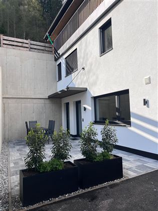 Een modern gebouw met een klein terras en plantenbakken. Het gebied is helder en vriendelijk ingericht, met meubels om te ontspannen.