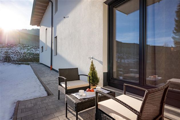 A cozy terrace with modern garden furniture and a beautiful view. The sun is shining on the snow-covered ground.