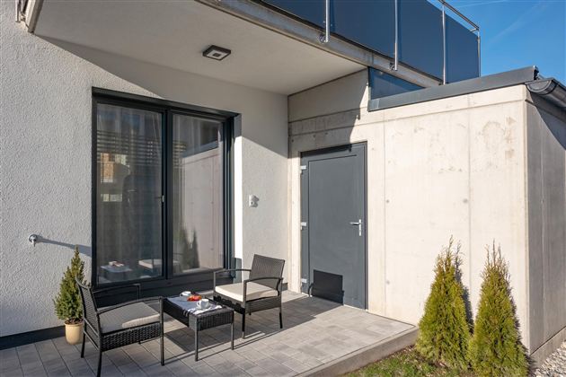 A modern terrace with two chairs and a table. In the background, there is a gray wall and large windows.