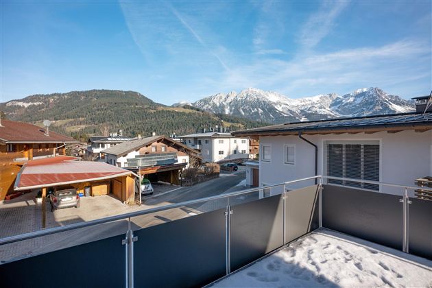 A beautiful view of snow-covered mountains and a picturesque alpine landscape. The sun shines over the rooftops of the houses in the area.